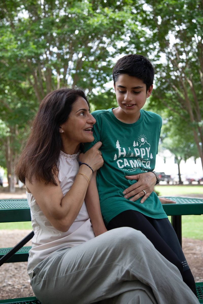 A mother and her teenage son sit together on a park bench.